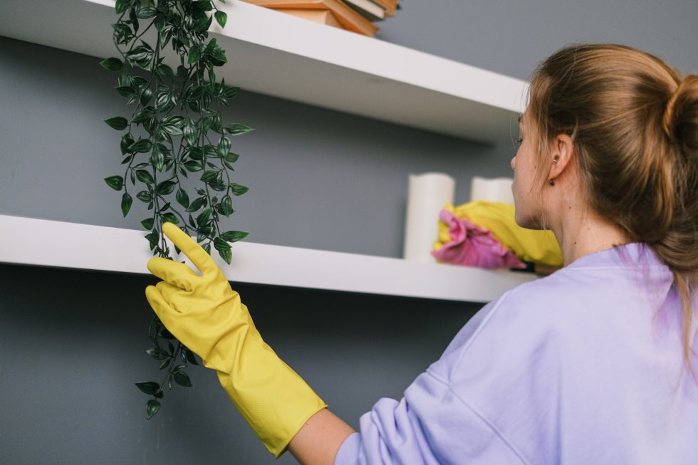 A woman in yellow gloves cleaning the shelves.