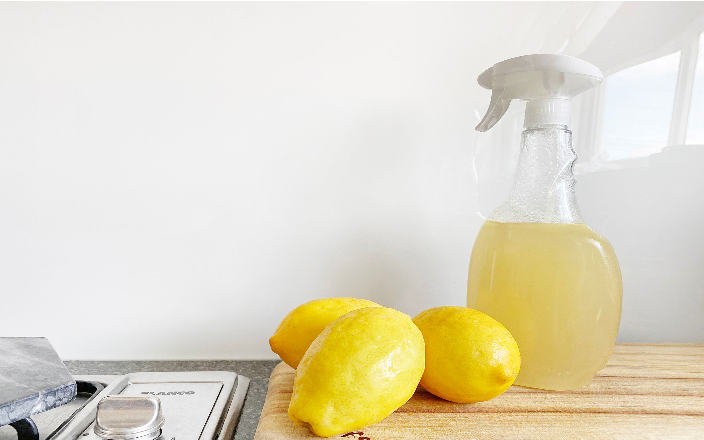 A wooden cutting board with lemons and spray bottle.