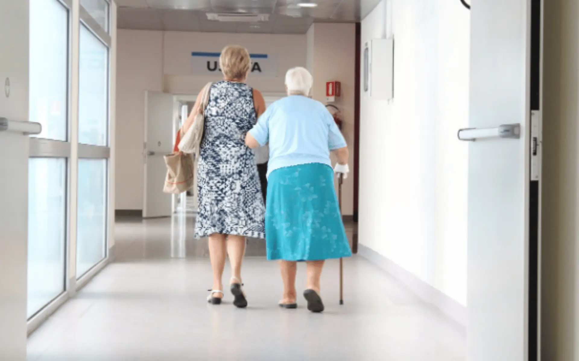 Two women walking down a hallway with one holding onto the other 's arm.