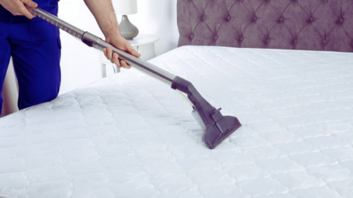 A person using a vacuum to clean the mattress.