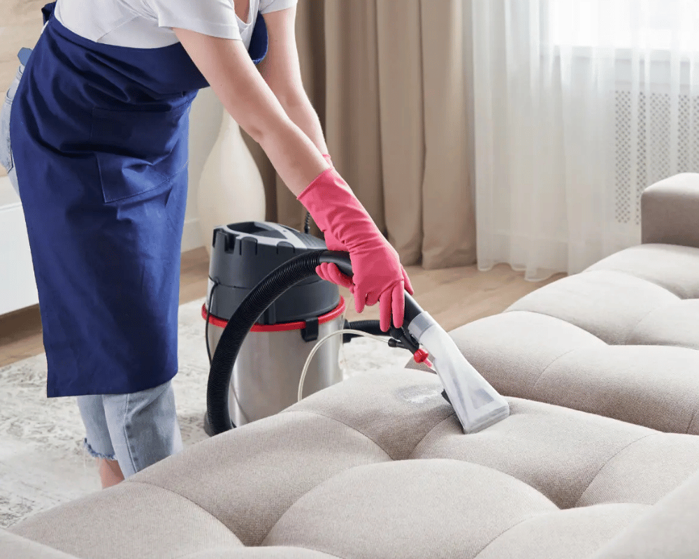 A person in pink gloves cleaning furniture with a vacuum.