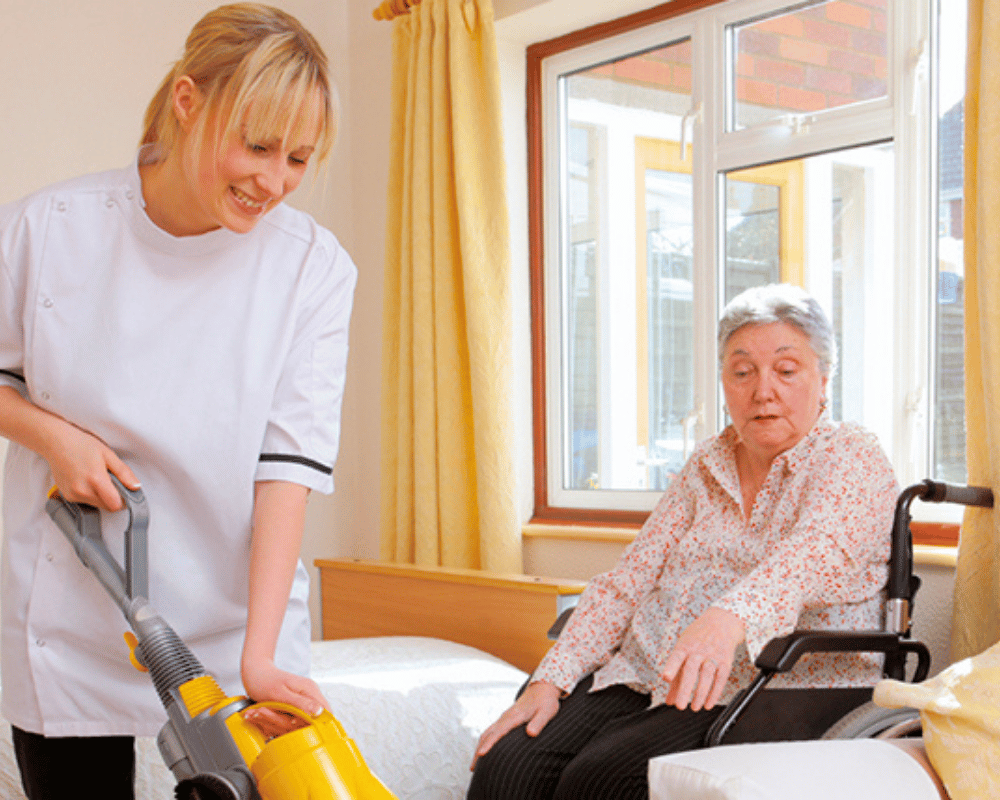 A woman is helping an elderly person use a vacuum.