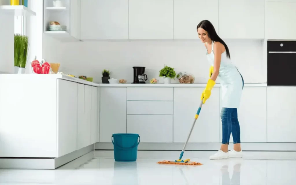 A woman in the kitchen cleaning with a mop